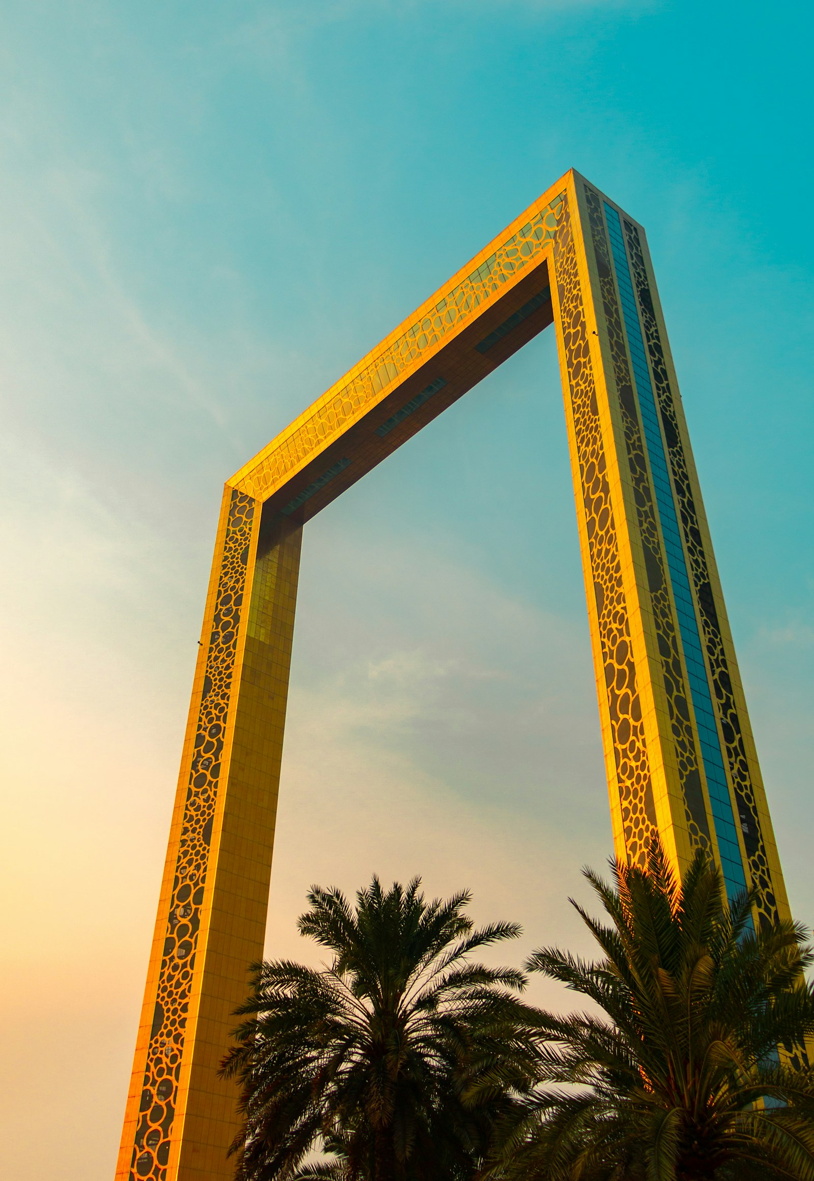 The Dubai Frame in gold at sunset, palms in the foreground